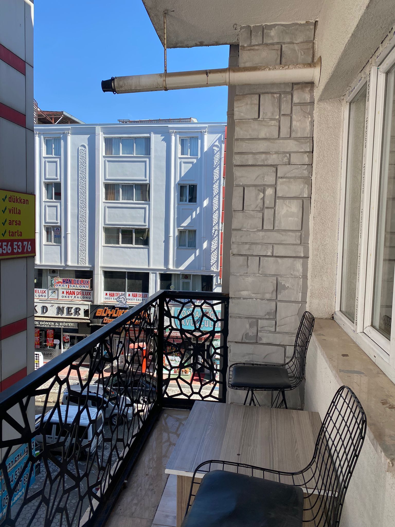 A balcony with a table and chairs, a metal railing, and a view of a building with multiple windows and signs.