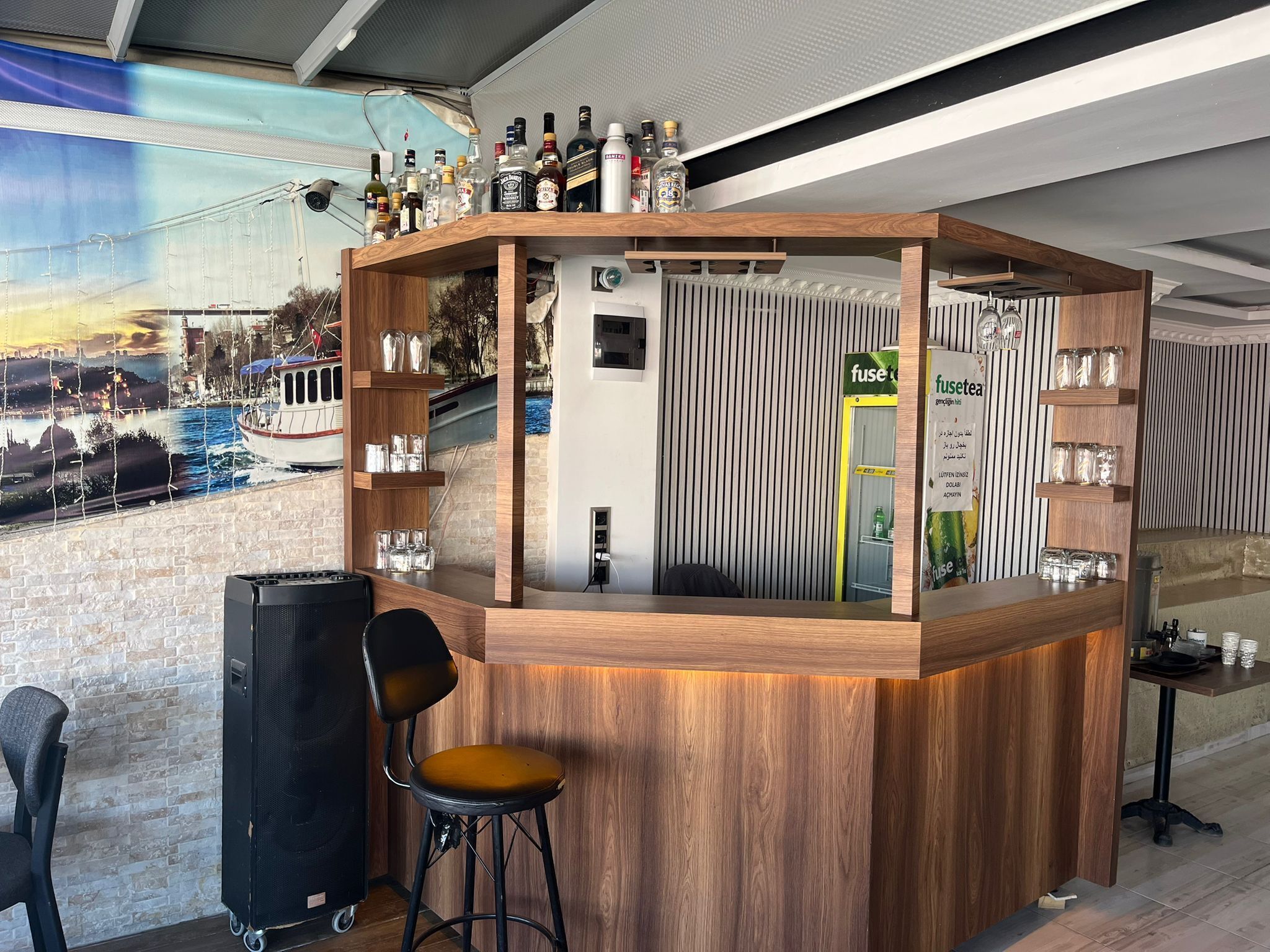 A bar area with a wooden counter, shelves with bottles, a water dispenser, and a chair.