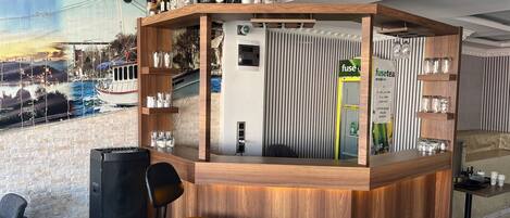 A bar area with a wooden counter, shelves with bottles, a water dispenser, and a chair.