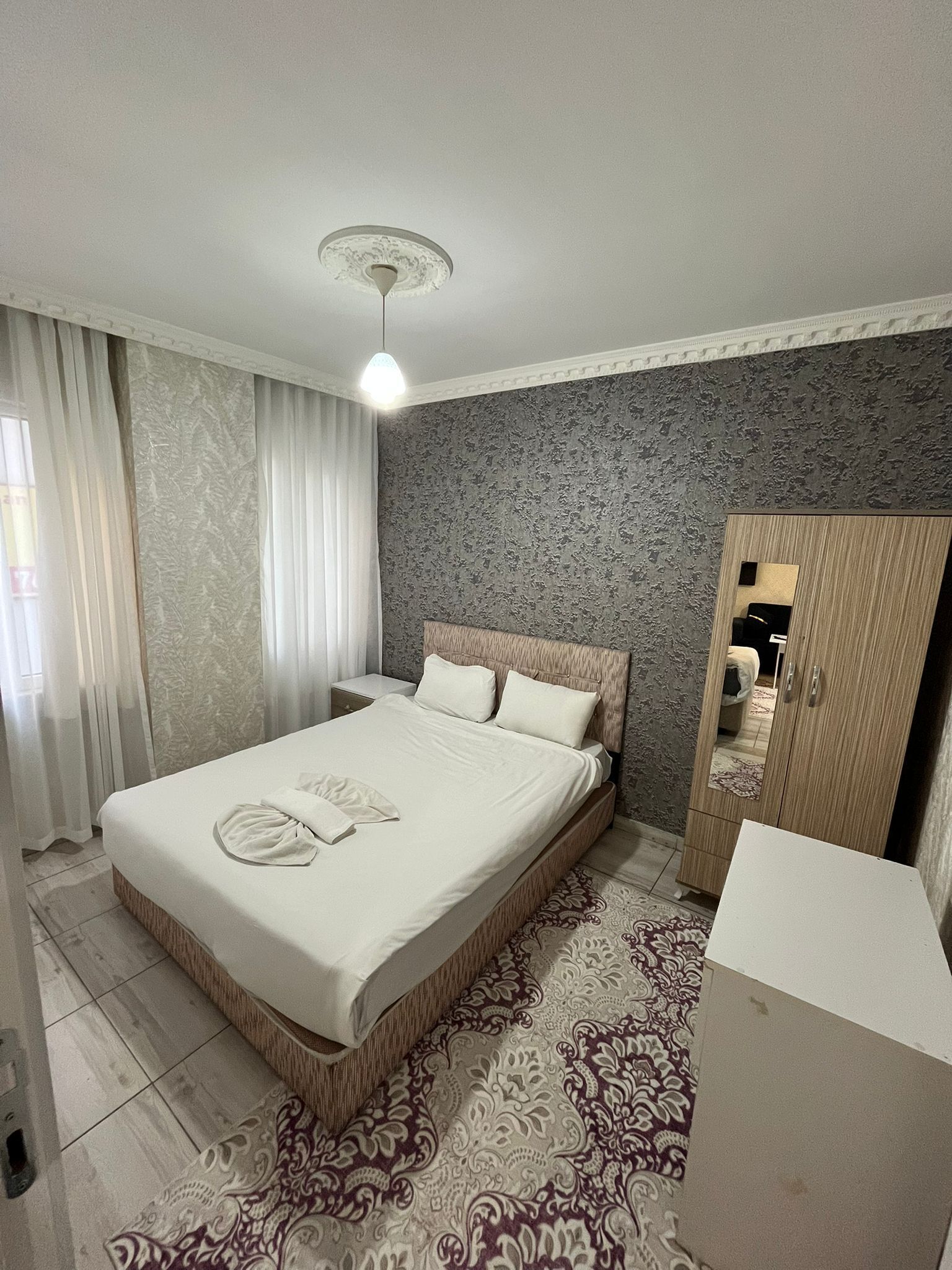 A hotel room with a large bed, a bedside table, a wardrobe, and a mirror.