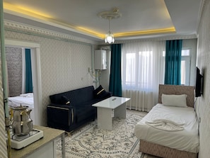 Ein Hotelzimmer mit Bett, Sofa, kleinem Tisch, Wasserkocher und Fernseher.