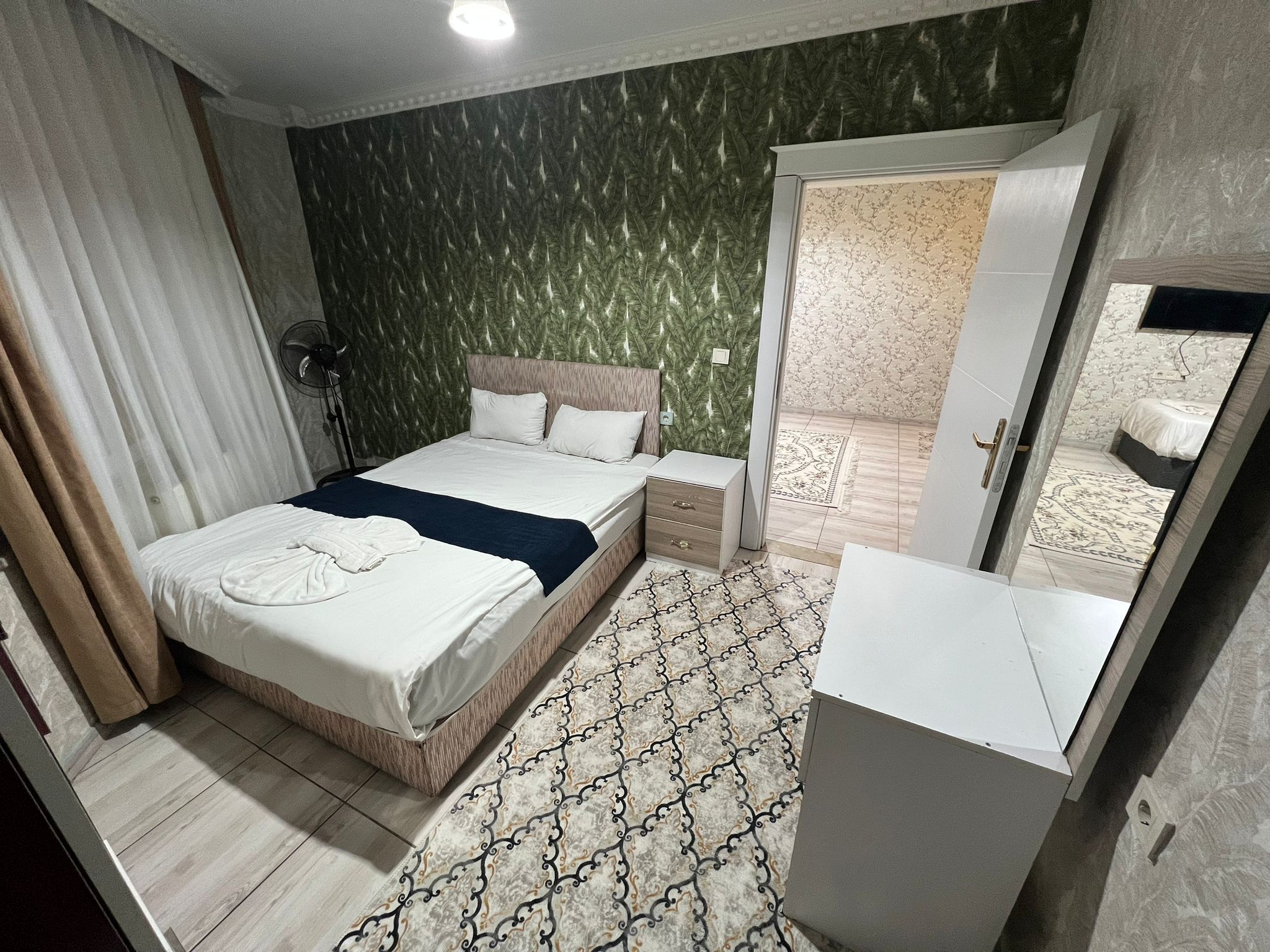 Een hotelkamer met een bed, nachtkastjes, een kledingkast, een spiegel en een kamerbreed tapijt.