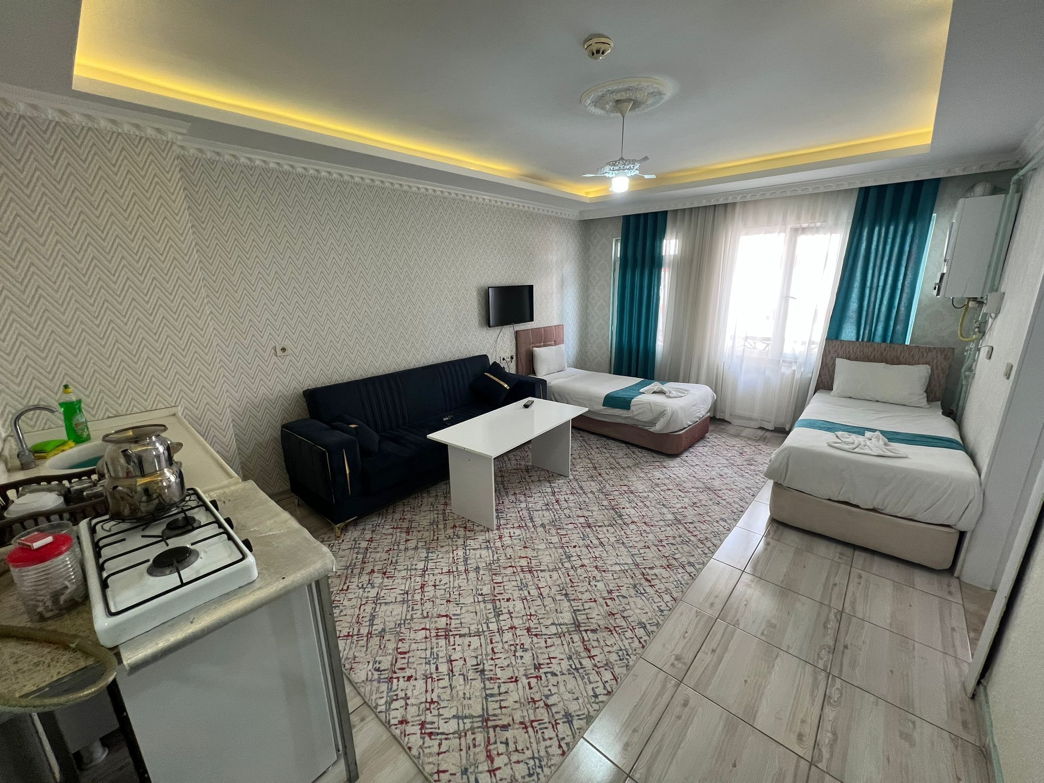 A hotel room with a kitchenette, a sofa, a bed, a flat-screen TV, and a ceiling fan.