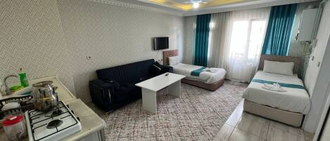 A hotel room with a kitchenette, a sofa, a bed, a flat-screen TV, and a ceiling fan.