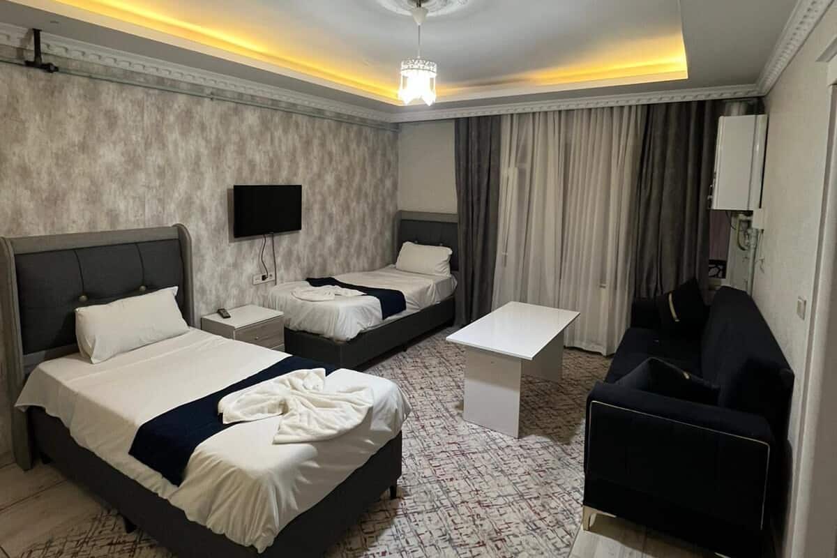 A hotel room with two beds, a desk, a chair, a flat-screen TV, and a chandelier.