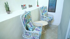 A small outdoor seating area with two wicker chairs and a table, a potted cactus, and a motivational poster on the wall.