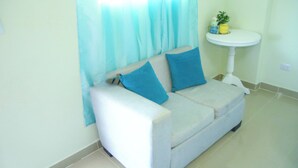 A white sofa with blue cushions, a white pedestal sink, and a small plant on the sink.