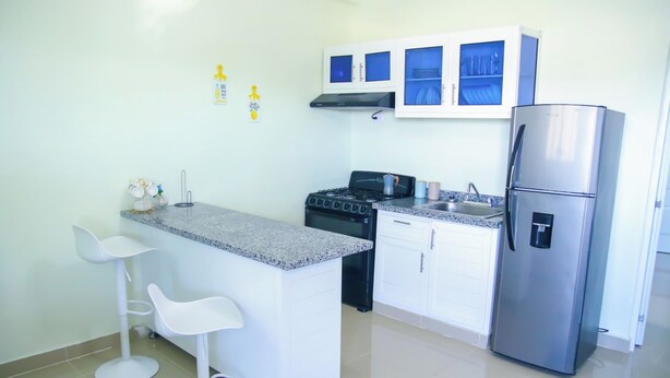 A compact kitchen with white cabinets, a stainless steel refrigerator, a gas stove, and two white bar stools.