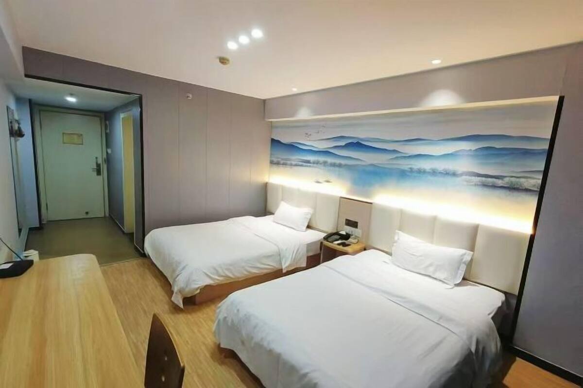 A hotel room with two beds, a desk, and a painting on the wall.