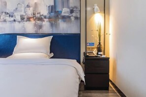 A hotel room with a bed, a nightstand with a lamp, and a cityscape painting on the wall. - 7 Days Inn (Zibo Zhou Village Gushangcheng Street) (Zibo)