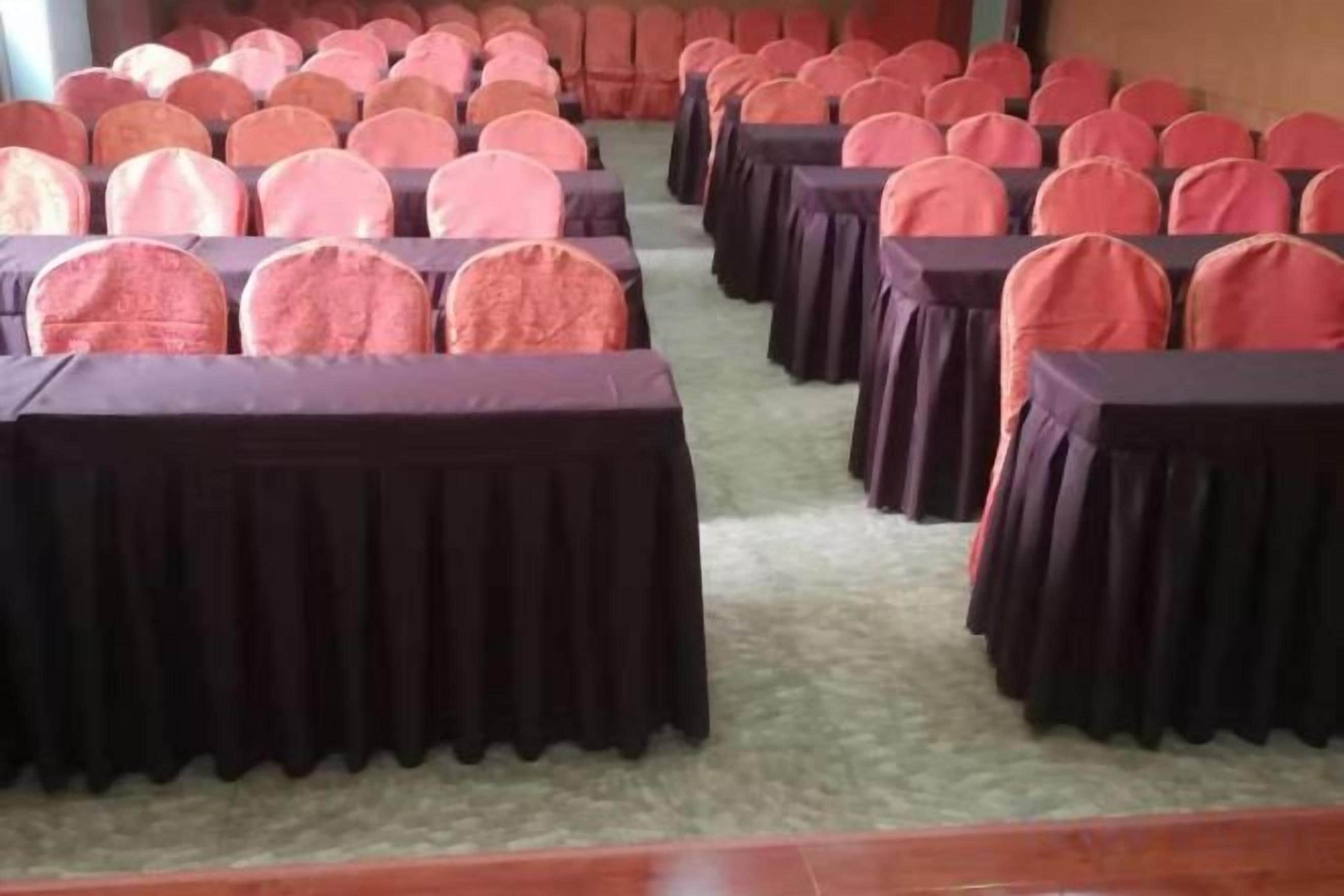A conference room with rows of tables and chairs, carpeted floor, and a plain wall.