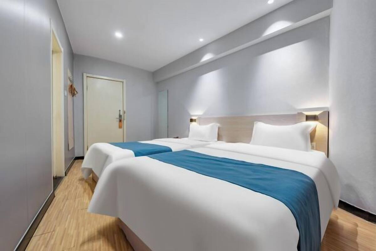 A hotel room with two beds, a wooden floor, and a white door.