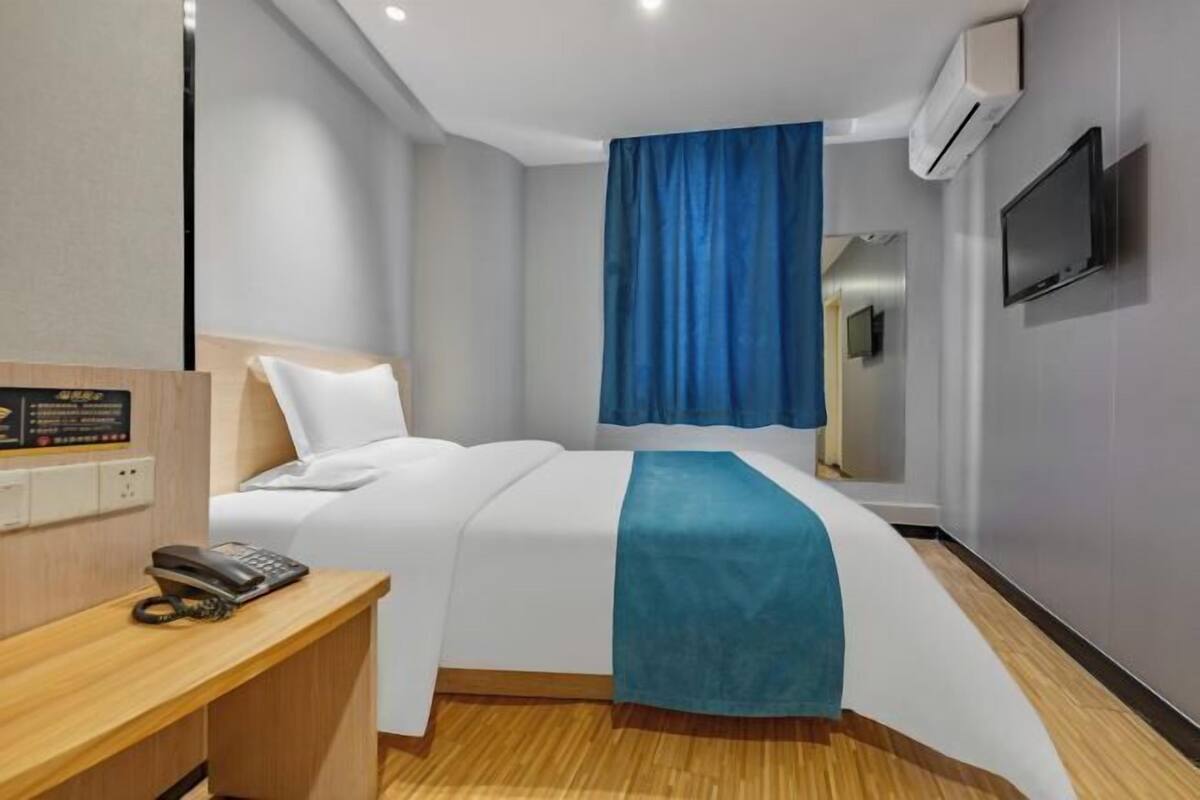 A hotel room with a bed, a desk with a telephone, a TV, and an air conditioning unit.