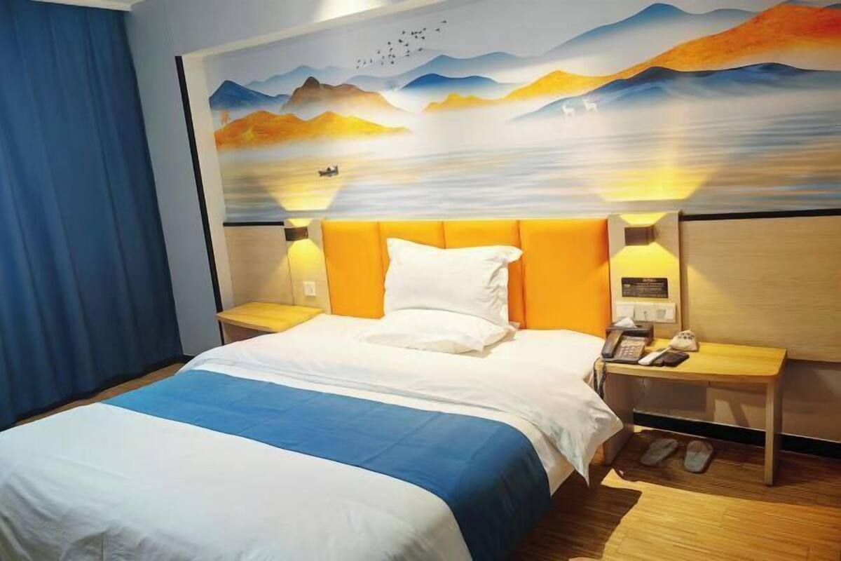 A hotel room with a bed, two bedside tables, a nightstand, a wall mural, and a blue curtain.