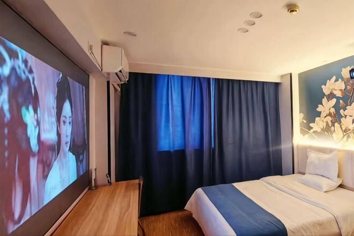 A hotel room with a bed, a TV screen, a desk, and a window with curtains.