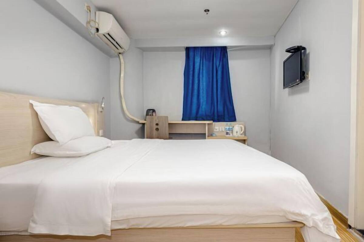 A small, neatly arranged bedroom with a bed, a bedside table, a TV, and an air conditioning unit.