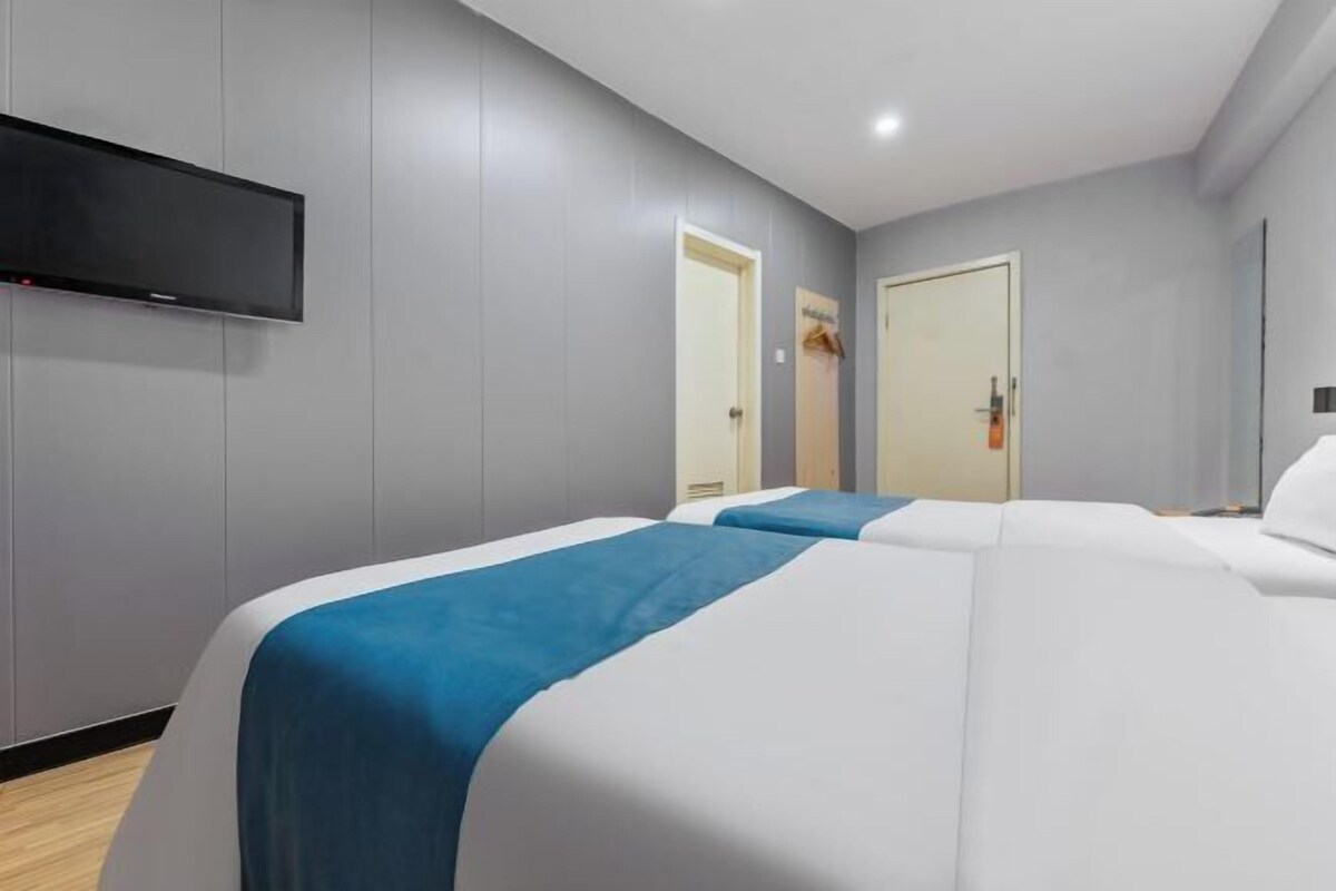 Habitación de hotel con dos camas, un televisor de pantalla plana montado en la pared y una puerta que da al baño.