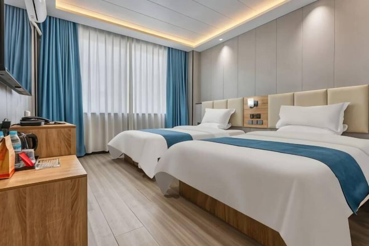 A hotel room with two beds, a wooden desk, a nightstand, and a window with curtains.