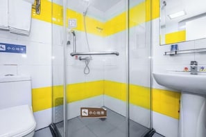Un baño pequeño y de colores vivos, con azulejos amarillos y blancos, cabina de ducha de vidrio, lavabo blanco y un inodoro.