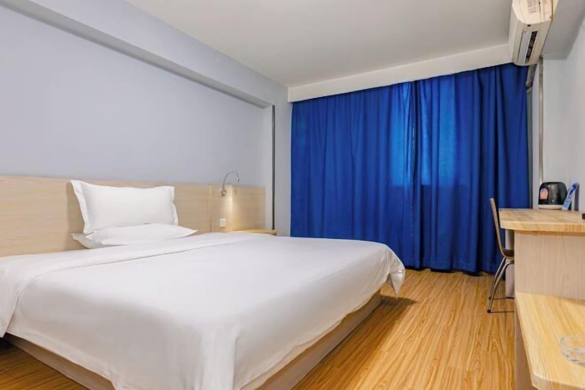 Una habitación de hotel con una cama, un escritorio, una silla y una ventana con cortinas azules.