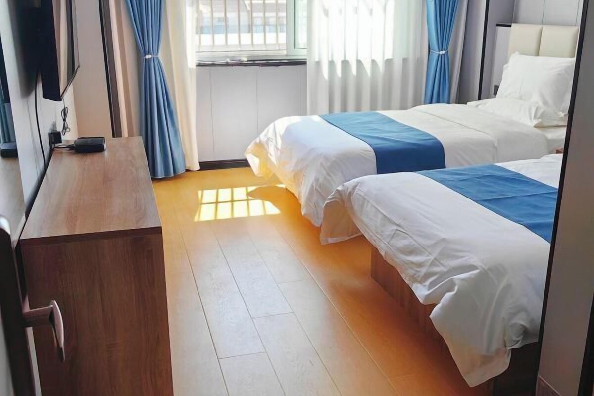 Una habitación de hotel con dos camas, un aparador de madera, un televisor y una ventana con cortinas.
