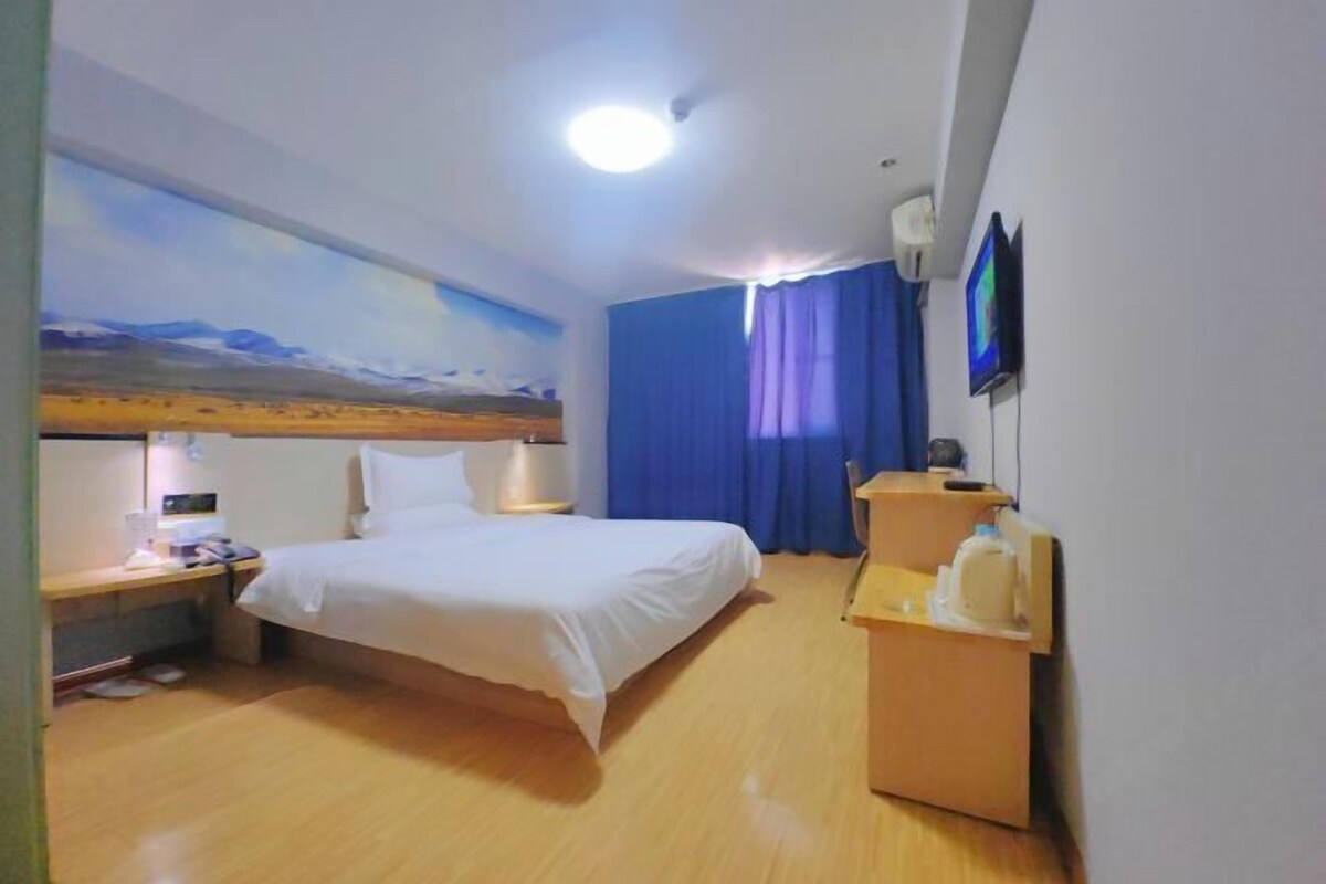 Habitación de hotel con cama, escritorio, televisión de pantalla plana, mesita de noche y televisor montado en la pared.