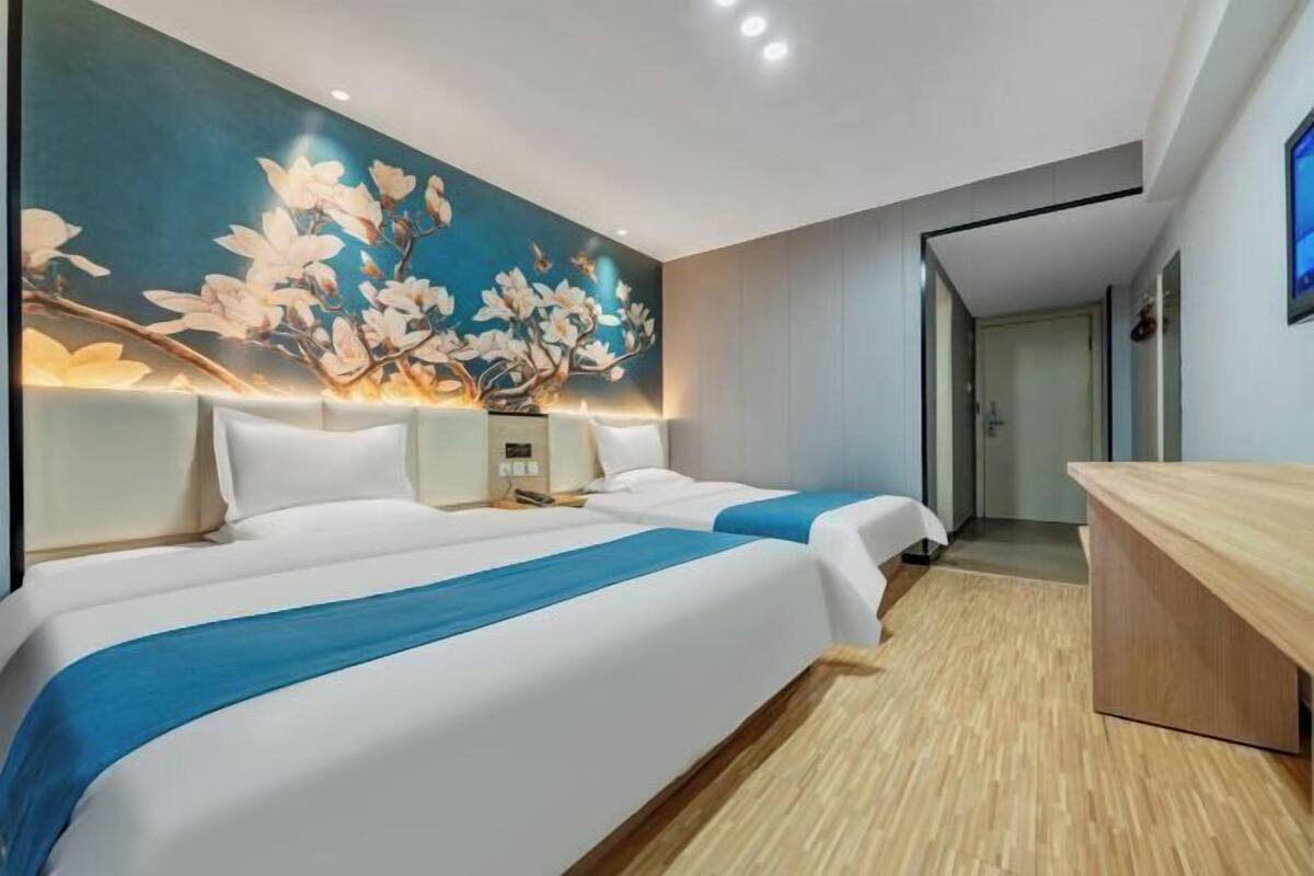 A hotel room with two beds, a wooden desk, and a wall mural.