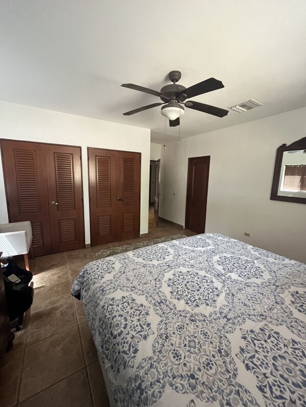 A bedroom with a bed, a ceiling fan, a dresser, and a door.