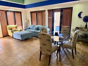 Un vaste espace de vie comprenant un canapé bleu, un fauteuil jaune, une table à manger en verre et un mur décoratif en briques.