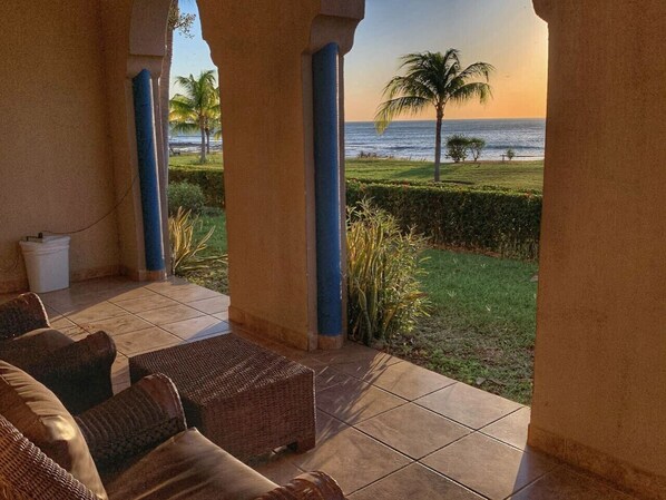 Un patio cubierto con mobiliario de mimbre, vista al océano y palmeras.