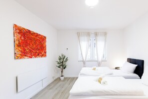 Une chambre d’hôtel avec deux lits, une grande peinture abstraite, une plante en pot et une fenêtre avec des rideaux.