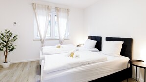 Hotellihuone, jossa on kaksi sänkyä, ruukkukasvi, ikkuna, jossa on verhot, ja pieni pöytä.