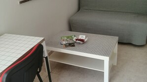 Ein kleiner, ordentlicher Raum mit einem weißen Tisch, einem schwarzen Stuhl, einem grauen Sofa und einer Karte an der Wand.