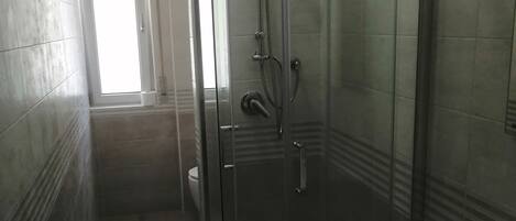 Un baño moderno con ducha de vidrio, un lavamanos blanco y paredes con azulejos.