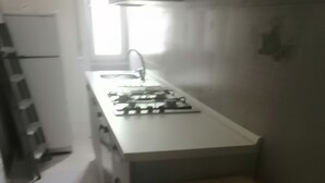 Eine kleine Küche mit weißer Arbeitsplatte, Spüle und Herd. Im Raum befinden sich eine Bank und ein Stuhl.