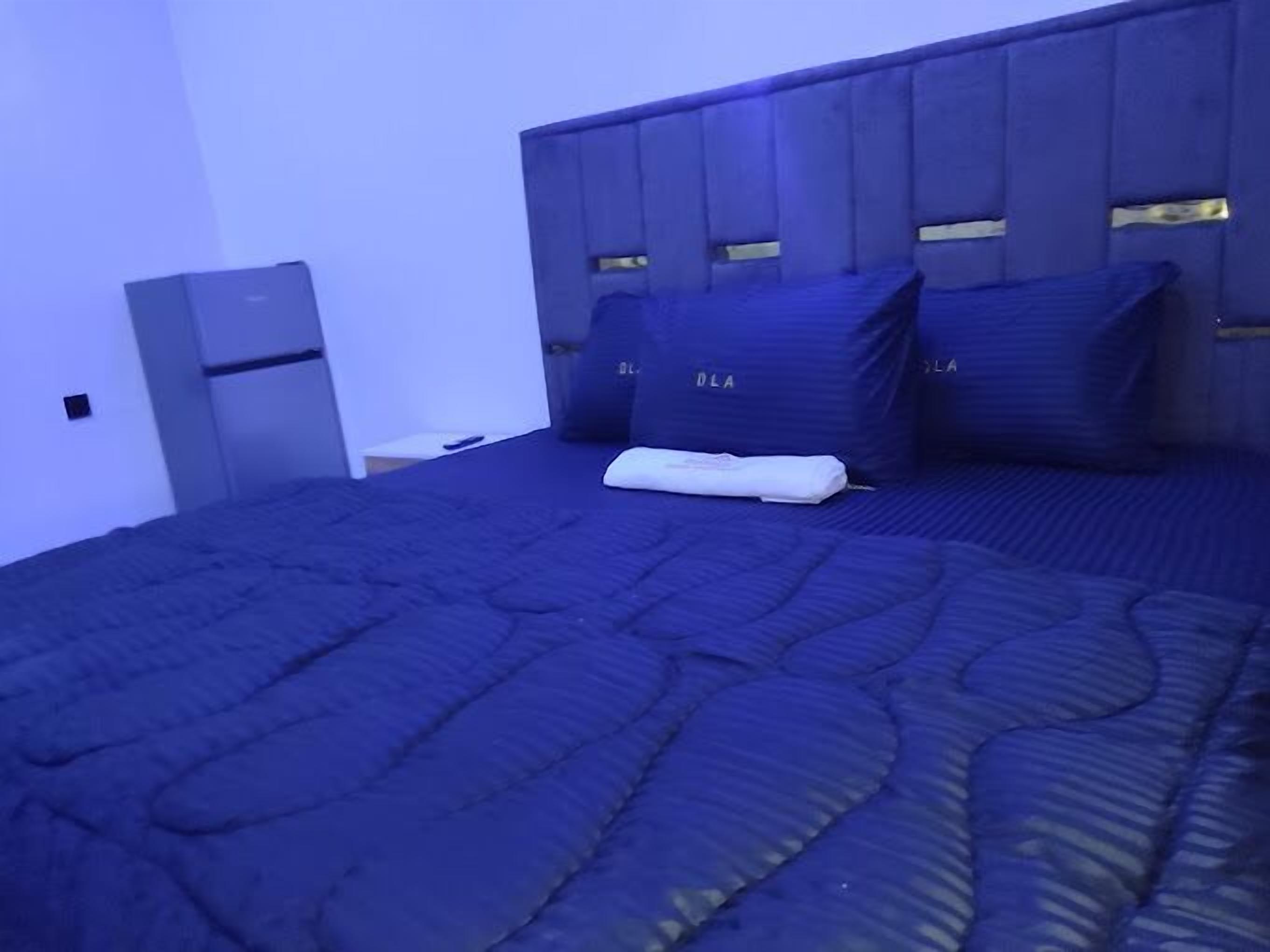 Cama bem arrumada com colcha azul escura e travesseiros com a etiqueta 'DLA'.