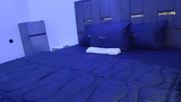 Cama bem arrumada com colcha azul escura e travesseiros com a etiqueta 'DLA'.