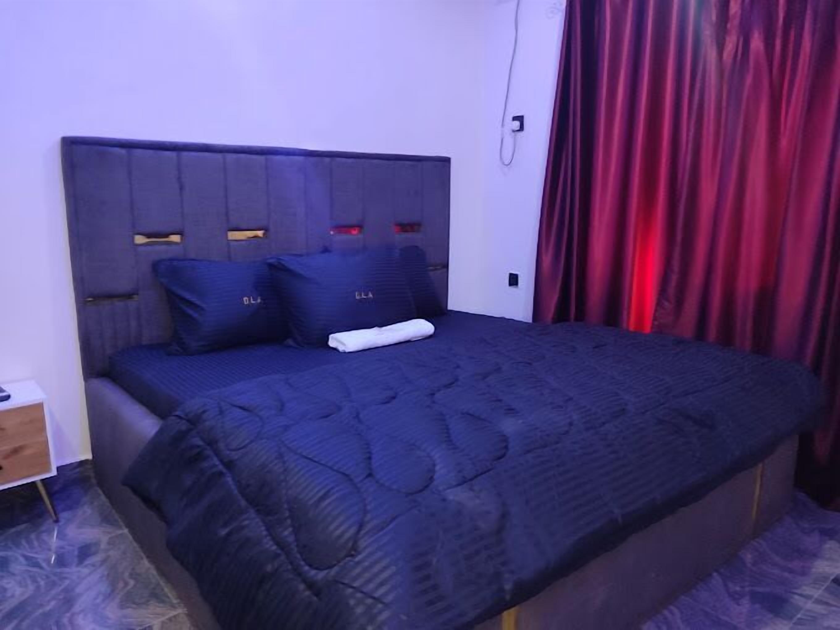 Una cama individual con cabecera azul oscuro y almohadas a juego, una toalla blanca y una cortina roja.
