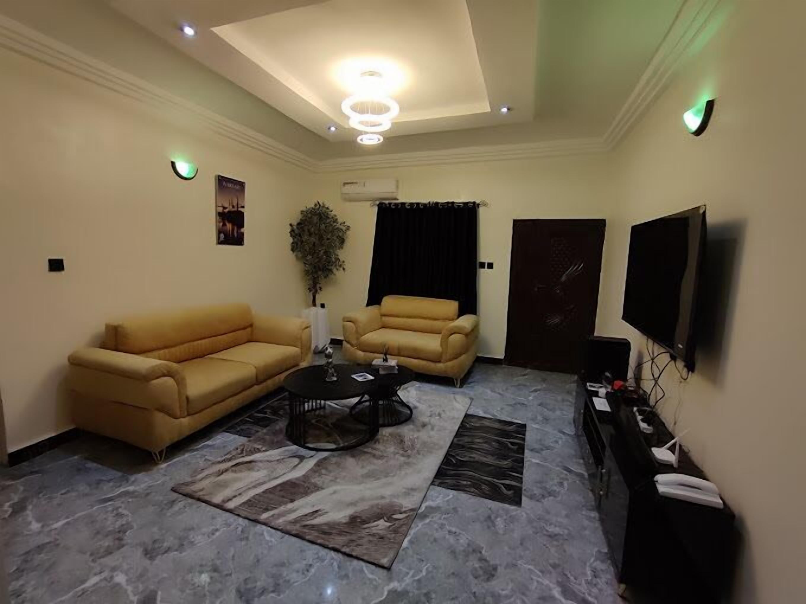 Un salon avec un canapé beige, un fauteuil plus petit, une table basse et un téléviseur posé sur un meuble.