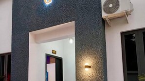 Una entrada de edificio con fachada texturizada, un letrero sobre la puerta y una unidad de aire acondicionado pequeña a la derecha.