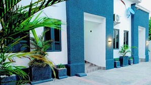 Un edificio moderno con fachada azul, ventanas amplias y plantas en macetas a lo largo del paseo.