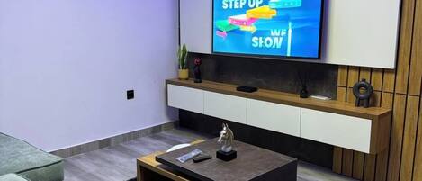 A modern living room with a flat-screen TV mounted on the wall, a wooden cabinet below, a black coffee table, and a grey sofa.
