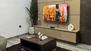 Una sala de estar moderna con un televisor de pantalla plana grande montado en la pared, una mesa de centro de madera oscura, una planta en maceta y un sofá color beige.