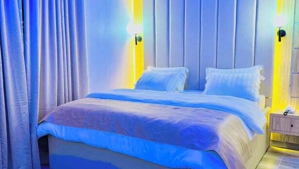 Un dormitorio moderno con una cama grande, una alfombra oscura y una mesita de noche con una lámpara.