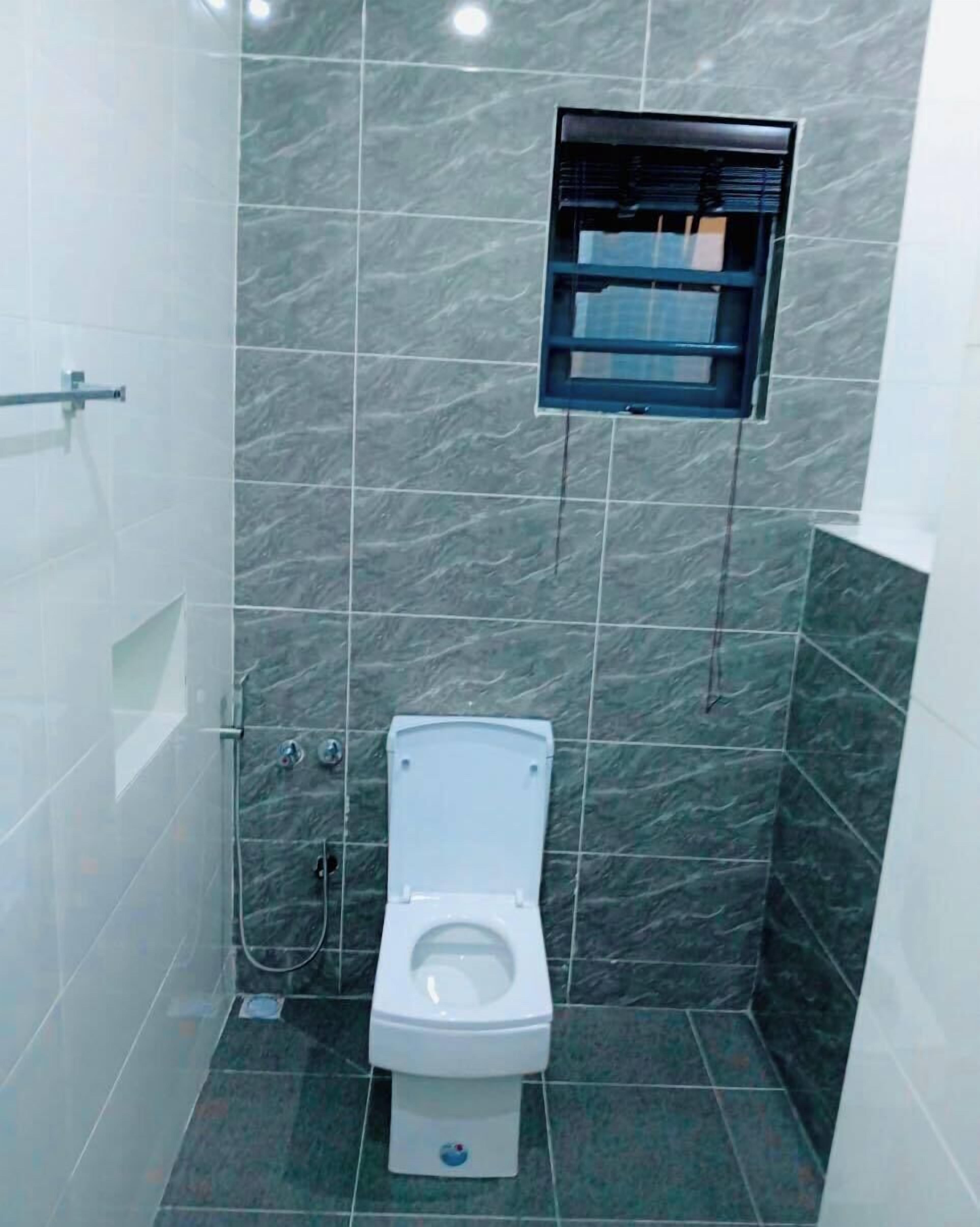 Une petite salle de bain moderne, équipée de toilettes, d’une douche et d’une petite fenêtre.