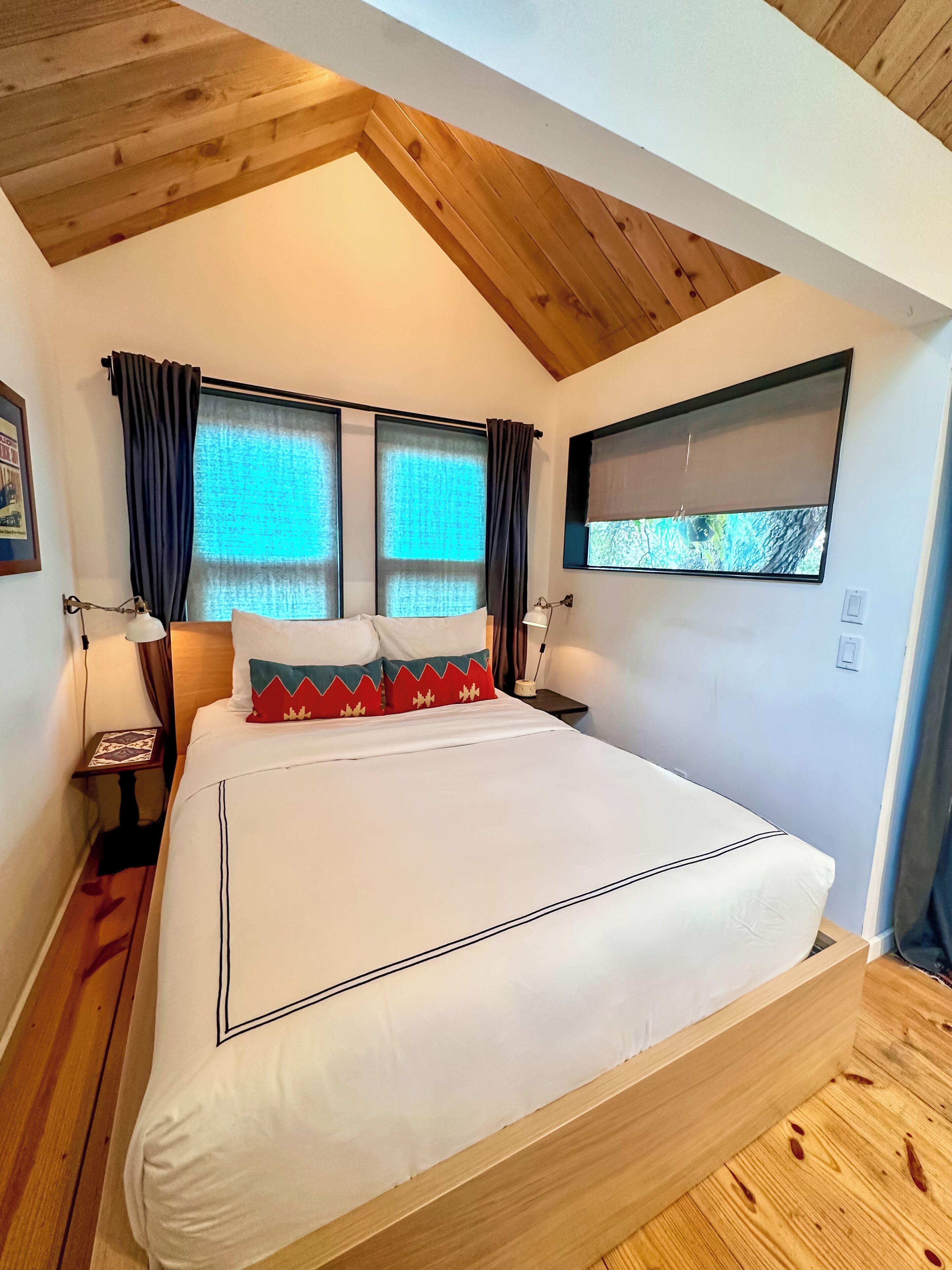 Een slaapkamer met een groot bed, twee nachtkastjes, een televisie aan de muur en een raam met gordijnen.