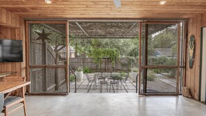 Een houten interieur met een schuifdeur die uitkomt op een terras buiten, met een tafel en stoelen.