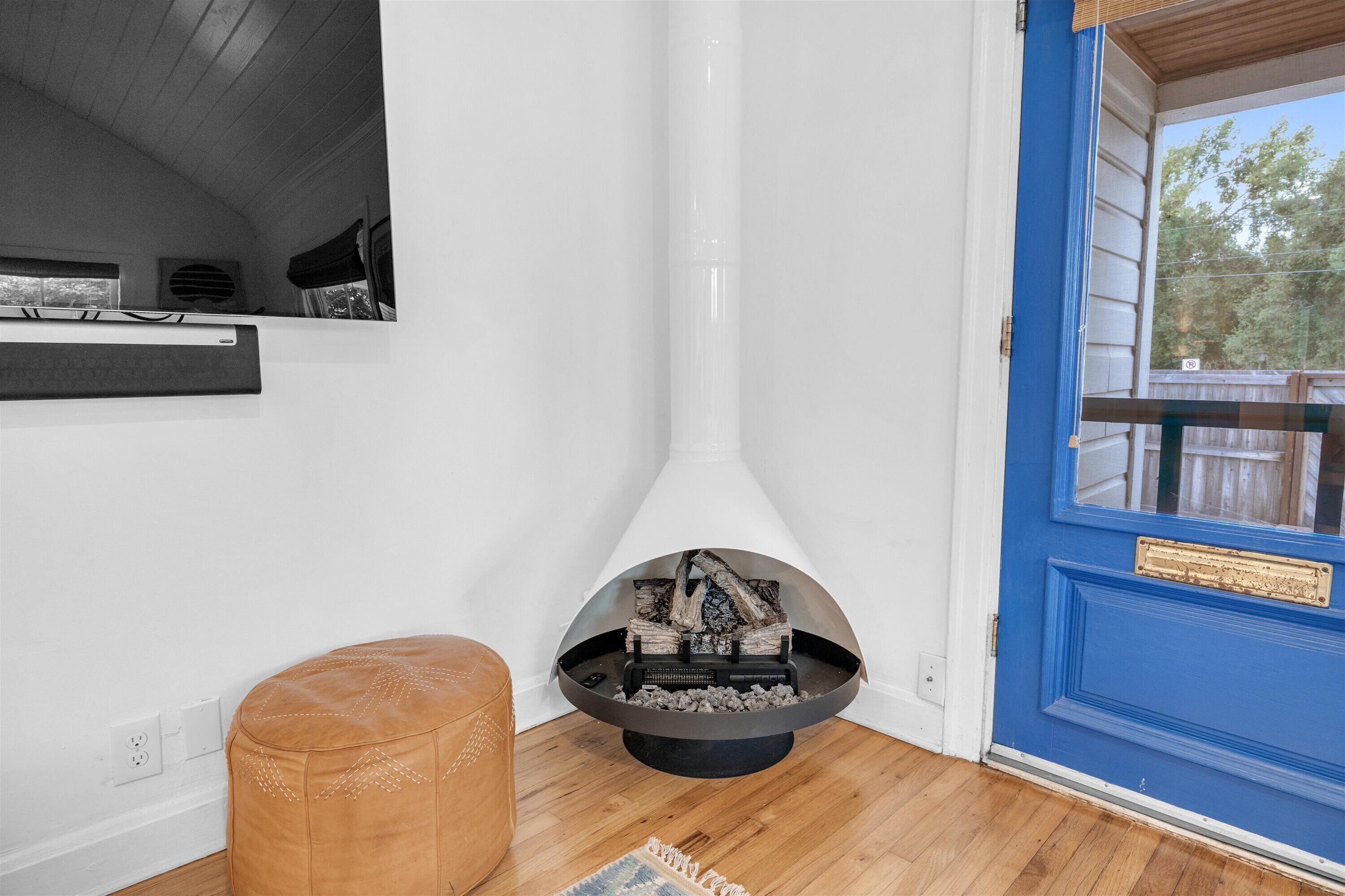 A corner room with a fireplace, a brown ottoman, and a blue door.