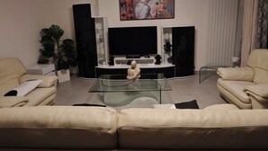 Una sala moderna con un televisor de pantalla plana, dos sofás, una mesa de centro de vidrio y una planta en maceta.