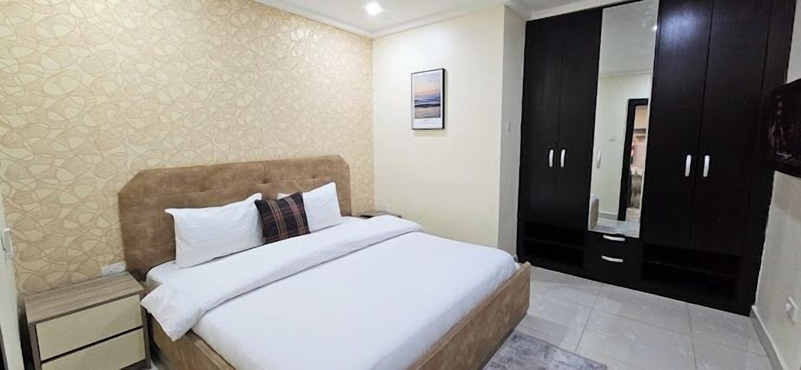 Un dormitorio con cama, mesita de noche, armario y un cuadro en la pared.